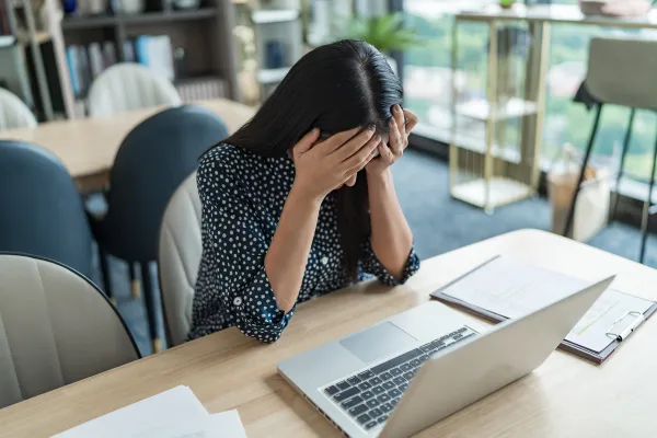 デスクでノートパソコンを前に、頭を抱えて業務の悩みに打ちひしがれる女性