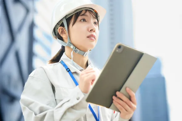 ヘルメットを着用し、建設現場でタブレット端末を確認する女性スタッフ